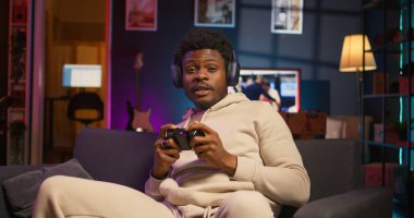 Afrika kökenli Amerikalı bir adam çatı katında video oyunu oynuyor, eğlence olsun diye kontrol cihazını tutuyor. Erkek oyuncu geceleri internet çok oyunculu oyunlara katılıyor. Kamera B.