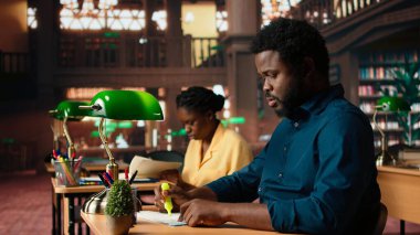 Siyahi üniversite öğrencisi önemli terimlerin altını çizerek önemli bilgileri ezberleyerek ders dersinin özetini öğrenmek için ilgili ifadeleri vurguluyor. Akademik kütüphane. Kamera A.