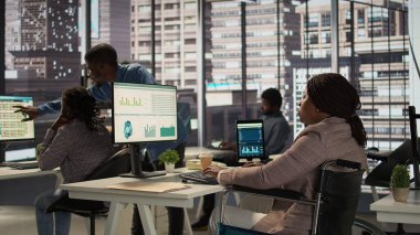 Siyahi yönetici tekerlekli sandalye kullanıcısı aylık raporların mali verilerini inceliyor ve doğru bir gelir dengesi sağlıyor. İş operasyonlarını engelli bir kadın çözüyor. Kamera B.