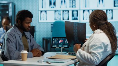 Afrika kökenli Amerikalı genç adam ve uzman tomografi ve röntgenleri gözden geçirip teşhis konulduktan sonra tedaviyi tartışıyorlar. Tıbbi pratisyen, yorumlama ve uzmanlık yapar. Kamera A.