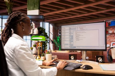 Ofisteki kadın bilgisayar ekranında UI 'ye bakıyor, programlama kodunu yazıyor ve çalıştırıyor. Kullanılan kodlama uygulaması UI modern apartmanda Afrika kökenli Amerikalı IT geliştiricisi yazma ve test kodu