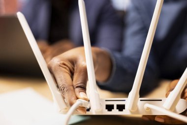 Genç siyahi kadın modemden LAN kablosunu çıkarırken erkek arkadaşı bilgisayarında sorun çözme kılavuzu okuyor. Wi-Fi bağlantı sorunlarını çözmek için sıfırlandı. Kapat..