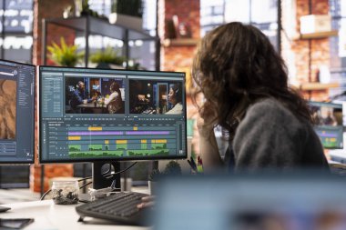 Ajans stüdyosunda çift monitörlü bir video düzenleyen video yapımcısı kadın zaman çizgisi düzenleme ve renk derecelendirme arasında birden fazla iş yapıyor. Profesyonel düzenleyici teknoloji araçları ve yazılım kullanır.