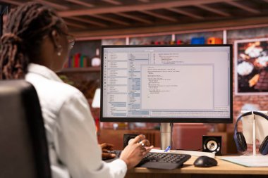 Merkez ofisteki uzaktan çalışan mühendis bilgisayar monitöründeki UI 'ye bakıyor, programlama kodunu yazıyor ve çalıştırıyor. Modern apartmanda kod yazmak ve test etmek için kodlama uygulaması kullanan kişi