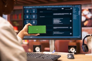 Ofisteki yapay zeka sohbet robotlarının video derslerine bakmak için akıllı telefon kullanan bir kadın. Yapay zeka LLM 'lerindeki görsel rehberlere bakmak için elinde yeşil ekran telefonu olan kişi.