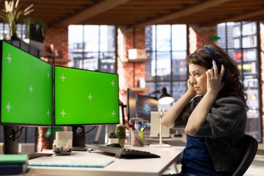 Kadın çalışan, yaratıcı ajans kurulumunda, yüksek teknoloji çalışma ortamında yeşil ekran modeli ve kulaklık kullanıyor. Modern çalışma alanı üretkenliği ve iş verimliliğini artırır.