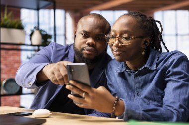 Evlerinden yapılan sanal bir çağrıya katılan dahili ofis kullanıcıları, atölyedeki iş arkadaşlarıyla birlikte akıllı telefon uygulamasını kullanarak. Afrika kökenli Amerikalı uzaktan kumandalı işçiler..