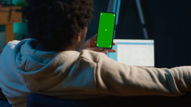 Kendine güvenen teknoloji kullanıcısı oturma odasında izole edilmiş bir maket görüntüsüne bakıyor. Kanepedeki uzaktan kumandalı işi ile rahatlıyor. Afrikalı Amerikalı mutlu yetişkin internette geziniyor. Kamera A.