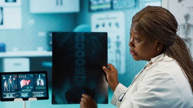 Tıbbi uzman teşhis için röntgen görüntülemesini açıklıyor, muayene sırasında tarama yorumu yapıyor. Afrikalı Amerikalı kadın sıhhiyeci erkek müşteriye geri bildirim yapar. Kamera A.