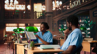 Eğitimdeki Afrikalı Amerikalı hemşireler tıp fakültesi ödevleri ve notları gözden geçiriyorlar, birlikte öğreniyorlar ve kampüs kütüphanesinde sınavlara hazırlanıyorlar. Tıp kariyeri için sağlık muayenehanesi. Kamera A.