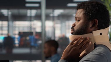 Boyun yaralanmasından muzdarip siyah genel müdür rahim boynu köpüğü giyer ve masasında rahatsız edici bir pozisyonda mücadele eder. Analizci günlük işlerini çözmeye çalışıyor ama acı çekiyor. Kamera A.