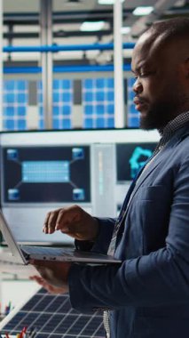 Dikey video Neşeli Fotovoltaik bitki uzmanı ofiste dayanıklılık ve performans alanında yenilikçi buluşlar üzerinde çalışıyor. Neşeli Afrikalı Amerikalı araştırmacı güneş panelleri için test materyalleri