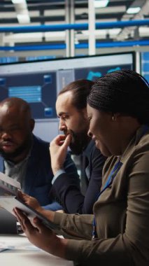 Dikey video fabrikası yöneticisi endüstriyel santralde otomasyon teknolojisi entegre etme üzerinde çalışıyor, cihaza bakıyor. Afro-Amerikalı kadın, iş modeli verilerini tablet üzerinde analiz ediyor, üretimi genişletiyor.