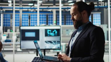 Güneş panellerindeki insan portresi güneş pillerinin verimliliğini artırmak için dizüstü bilgisayar kullanıyor. Fotovoltaik fabrikası araştırma ve geliştirme uzmanı not defteri kullanıyor, yeşil enerji çözümleri üzerinde çalışıyor, kamera A