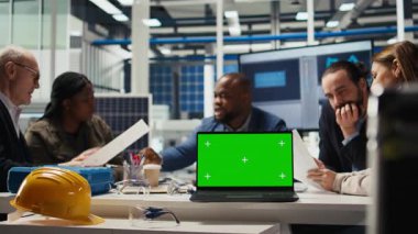 Fabrika mühendisleri kroma anahtar dizüstü bilgisayar kullanarak üretim planlarını rafine ediyorlar. Uzmanlar, izole ekran defteri ve kamera A kullanılarak prototipler için endüstriyel fabrika yapılandırmalarını özetliyorlar.