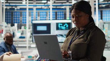 Araştırmacının portresi güneş pili prototiplerini enerji üretimini optimize etmek için dizüstü bilgisayar kullanarak analiz eder. Gülümseyen Afro-Amerikan güneş panelleri yenilikçi üretim teknolojisi geliştiren bitki uzmanları, kamera A