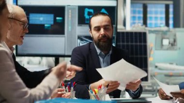 İş adamları, otomasyon teknolojisinin güneş paneli üretim süreçlerine entegrasyonunu tartışmak üzere yatırımcılarla bir araya gelerek evrak ve şemalara, kamera B 'ye bakıyorlar.