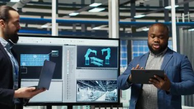 Fabrika yöneticileri yatırımcıların önünde satış yapıyor, üretim hatlarının planlarını gösteriyorlar. Endüstriyel fabrika yapılandırmalarını hissedarlara sunan yönetim, kamera B