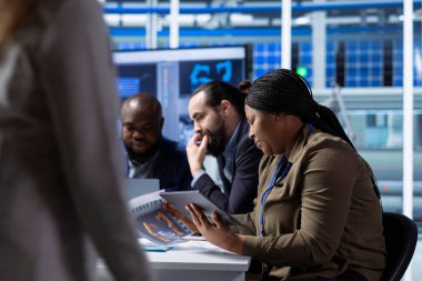 Photovoltaics fabrika yöneticileri tablet kullanarak şematiklere bakıyor, tesis zeminini yükseltiyorlar. Afrika-Amerika güneş panelleri fabrika yöneticisi holding cihazı montaj hatlarının planlarına bakıyor