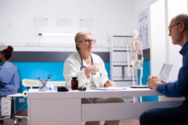 Yaşlı kadın hekim, sağlık sonuçlarını dikkatlice izah ederek ve tedaviyi tartışarak tıp bürosundaki kıdemli adama danışıyor. Emekli doktor, klinikteki hasta emekli erkek hastayla konuşuyor..