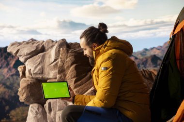 Trekker, sakin dağ manzarası ve açık gökyüzünün macerayı ve azmi simgelediği izole edilmiş taklit ekranın yanındaki panoramik manzarayı alıyor. Teknolojik seyahat tutkusu.