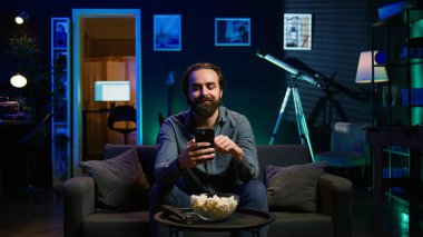 Adam gece geç saatlerde evinde kanepede oturmuş RGB 'deki akıllı telefondan arkadaşlarına mesaj atıyor. Arkadaşlarıyla sohbet etmek için cep telefonu kullanan kişi, sıcak neon ışıklı bir apartman dairesinde, B kamerasında.