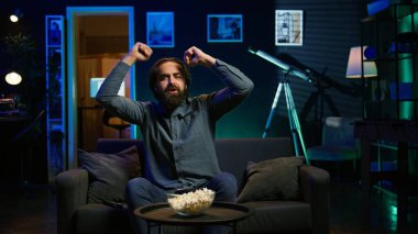 Coşkulu bir spor hayranı evinde canlı yayında en sevdiği takım golünü kutlamak için bağırıyor. Öforik adam bağırıyor, çılgınca el hareketi yapıyor, kaleye bayılıyor, kamera B