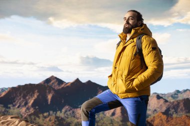 Kararlı gezgin, panoramik manzaranın macera ve kişisel gelişimi temsil ettiği bir dağ zirvesinin yalnızlığının tadını çıkarıyor. Açık hava teçhizatıyla yürüyüşçü rüzgarlı dağın tepesinde üşüyor..