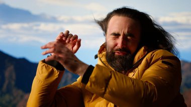 Erkek aktif gezgin, güzel dağ sırası vadisine hayran ama soğuk rüzgarlarla mücadele ediyor. Kamp alanındaki tehlikeli rüzgarlarla mücadele ediyor. Doğada gezinti tutkusu. Kamera B.