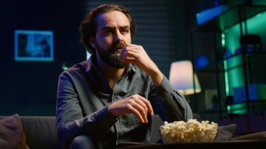 Tembel kanepe patatesi insanı düşüncesizce TV 'de programlar izliyor ve patlamış mısır yiyor, ekrana yakından bakıyor. Oturan adam aperatifleri yerken akılsızca eğleniyor, kamera A