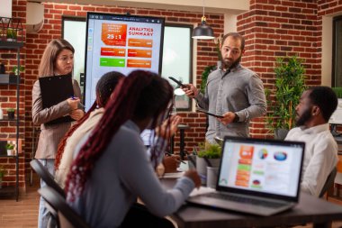 İş ekibi, dijital çizelgelerle pazarlama stratejilerini analiz ediyor. Ofisteki profesyoneller finansal analizi tartışıyor, çevrimiçi veri ve bilgi için modern teknolojiden faydalanıyorlar.