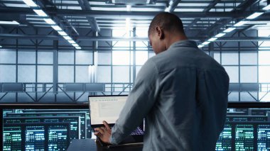 Sunucu odasında bilgisayar bilimci dizüstü bilgisayarda kodlama yapıyor, felaket kurtarma planları geliştiriyor. Veri merkezindeki Afrikalı Amerikalı adam notebook, kamera B kullanarak başarısız senaryoları test ediyor.