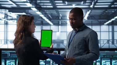 Veri merkezindeki bilgisayar bilimcileri taklit tablet kullanıyor, sunucu donanımlarını denetliyor, cihazları güncelliyor. Krom anahtar aygıtı, kamera B kullanılarak dengeli işlemleri sağlamak için işbirliği yapan bilişim iş arkadaşları