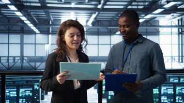 Veri Merkezi yöneticileri evrak dosyalarını okuyor, sistem tanılarını gözden geçiriyorlar. Sunucu çiftliği çalışanları bakım takvimlerine, belgelere ve siber güvenlik protokollerine bakıyor. Kamera B