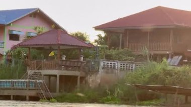 Tayland manzaralı su kanallarını ve köy evlerini keşfeden turist botu, bereketli ağaçlar ve doğanın barışçıl güzelliğiyle çevrili geleneksel bir Tayland nehrinde yüzen yelkenli..