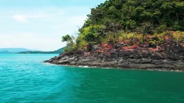 Küçük bir Tayland adası ve tropikal kıyı şeridinde yüzen bir teknenin havadan görünüşü. Mavi gökyüzü ve kıyı kayalıkları ile kıyıda sürüklenen yelkenlilerin bulunduğu sakin bir seyahat noktası..