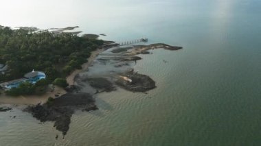 Resimli bir Tayland kıyı şeridine demirlemiş bir yelkenlinin insansız hava aracı çekimi, sakin turkuaz sularda dinlenen bir tekne, sahil kayalıkları ve altın kumlarla çevrili..