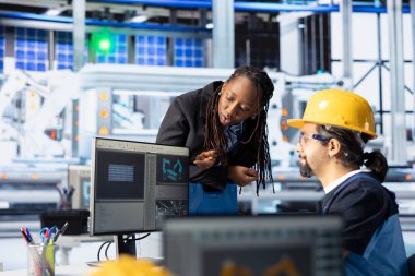 Fotovoltaik fabrikasında çalışan kadın ve erkek üretim akışını optimize ediyorlar. Sürdürülebilir enerji güneş panellerindeki Afrikalı Amerikalı yönetici bilgisayardaki fabrika izleme süreci