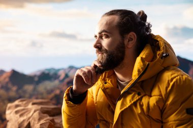Kararlı gezgin, panoramik manzaranın macera ve kişisel gelişimi temsil ettiği bir dağ zirvesinin yalnızlığının tadını çıkarıyor. Açık hava teçhizatıyla yürüyüşçü rüzgarlı dağın tepesinde üşüyor..