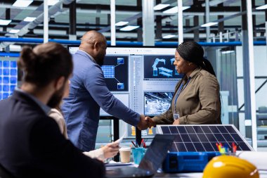 Güneş paneli fabrika yöneticisi imalat süreciyle ilgilenen yatırımcıyla el sıkışıyor. İnsan, üretim büyüme verilerini görmek ve el sıkışmak için fotovoltaik fabrikasını ziyaret eden hissedarları selamlıyor