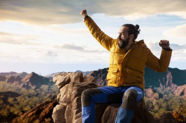 Trekker kollarını dağ sırasının tepesinde heyecan içinde uzatıyor, tırmanma başarısından gurur duyuyor ve tatmin oluyor. Genç yetişkinler azim ve hırslarını sergiler..