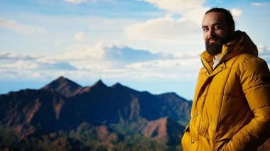 Sıcak kıyafetler giymiş yürüyüşçü zirveye tırmandıktan sonra bir dağın zirvesinde duruyor, engebeli tepelerin ve engin gökyüzünün nefes kesici manzarasına bakıyor. Manzaralı macera. Kamera A.