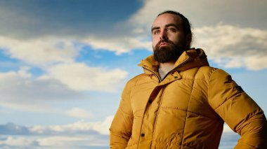 Doğa aşığı nefes kesen bir dağ sırasının kenarında duruyor, yükselen zirvelerin ve uçsuz bucaksız gökyüzünün manzaralı arka planına bakıyor. Macera ve açık hava keşiflerini seven genç bir adam. Kamera B.