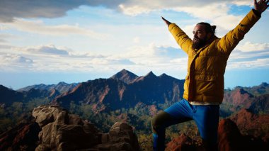 Gururlu kaşif dağın zirvesine ulaşır başarısından memnun ve memnun hisseder, dağların ve gökyüzünün manzaralı arka planından. Kendini geliştirme ve yeni ufuklar. Kamera A.