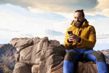 Doğa aşığı dağın tepesinde rahatlıyor telefonuyla manzaraya bakan manzaralı bir bakış açısıyla internete giriyor. Yürüyüşçü her zaman çevrim içi ve bağlı kalıyor, panoramik manzara.