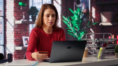 Gülümseyen bayan internet siparişini öderken kartını tutuyor. Ev ofisteki tabletle para aktarıyor ve alışveriş yapıyor. Kredi bakiyesini kontrol ettikten sonra memnun kadın alışverişi. Kamera A.