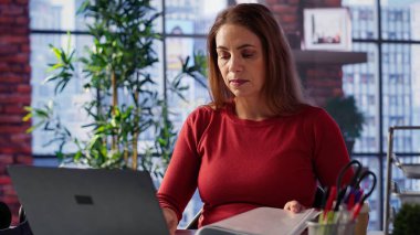 Olgun bir kadının şık çatı katında dizüstü bilgisayarı üzerinde odaklanması, serbest iş ve uzak sorumlulukları yönetirken internete bağlanması. Ev ofisinde web taraması. Kamera A.