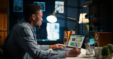 Serbest çalışan siyahi adam, evde birden fazla iş yapıyor. El yazısı notlar alıyor ve internette araştırma yapıyor. Verimliliği arttırmak için bir planlayıcının programını ve görevlerini yönetmek. Kamera A.