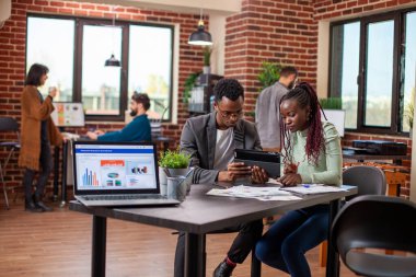 Siyahi girişimciler masada oturmuş dijital cihazla ilgili online iş makaleleri okuyorlar. Girişimcilik ofisinde yapılan ciddi bir tartışmada, iş ortakları belgeleri gözden geçirir ve tablet hakkındaki görüşleri paylaşırlar.