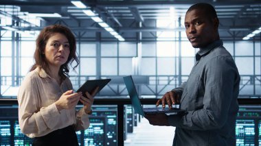 Sunucu odasında bilgisayar ve tablet kullanarak veri bilimcileri, güvenlik yamalarını çalıştırarak, güvenlik duvarı yapılandırmalarını doğrulayarak. Veri merkezinde ekipman hassasiyeti taraması yapan insanlar, kamera B